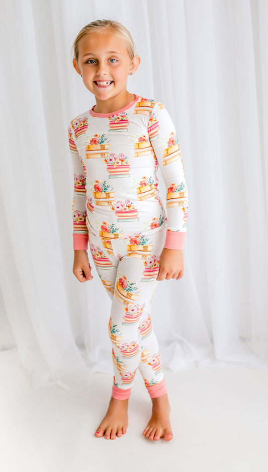 Child wearing a colorful two piece with floral prints and stacks of book on a white background with pink accents