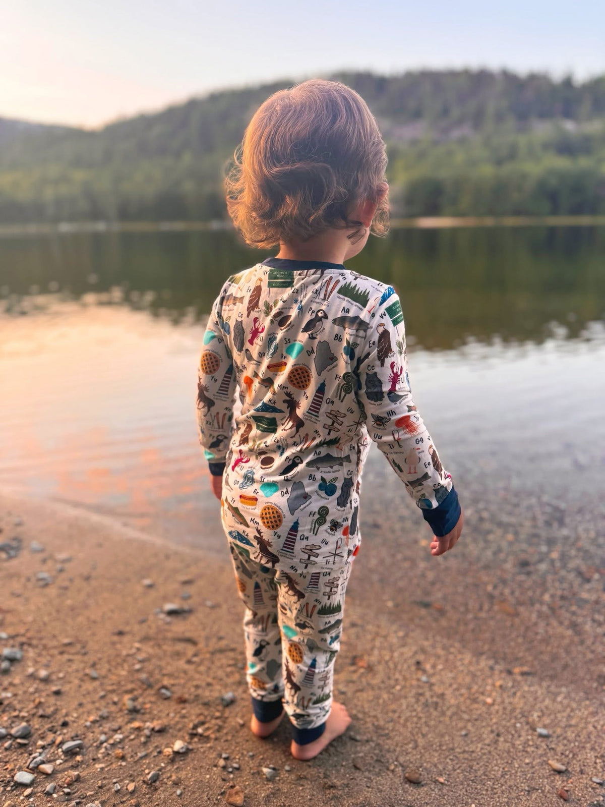 Child in pajamas standing by a in Maine with items on the pajamas to represent all the things that make up maine