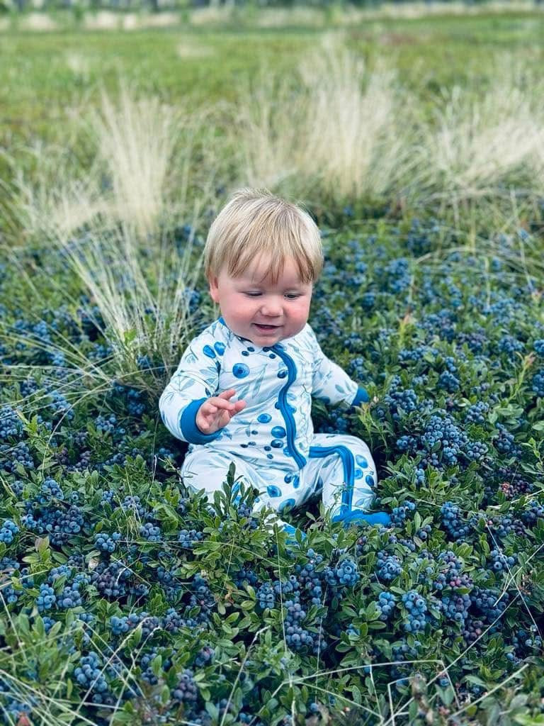 Baby wearing white zippy romper with maine blueberries all over and a darker blue on the cuffs