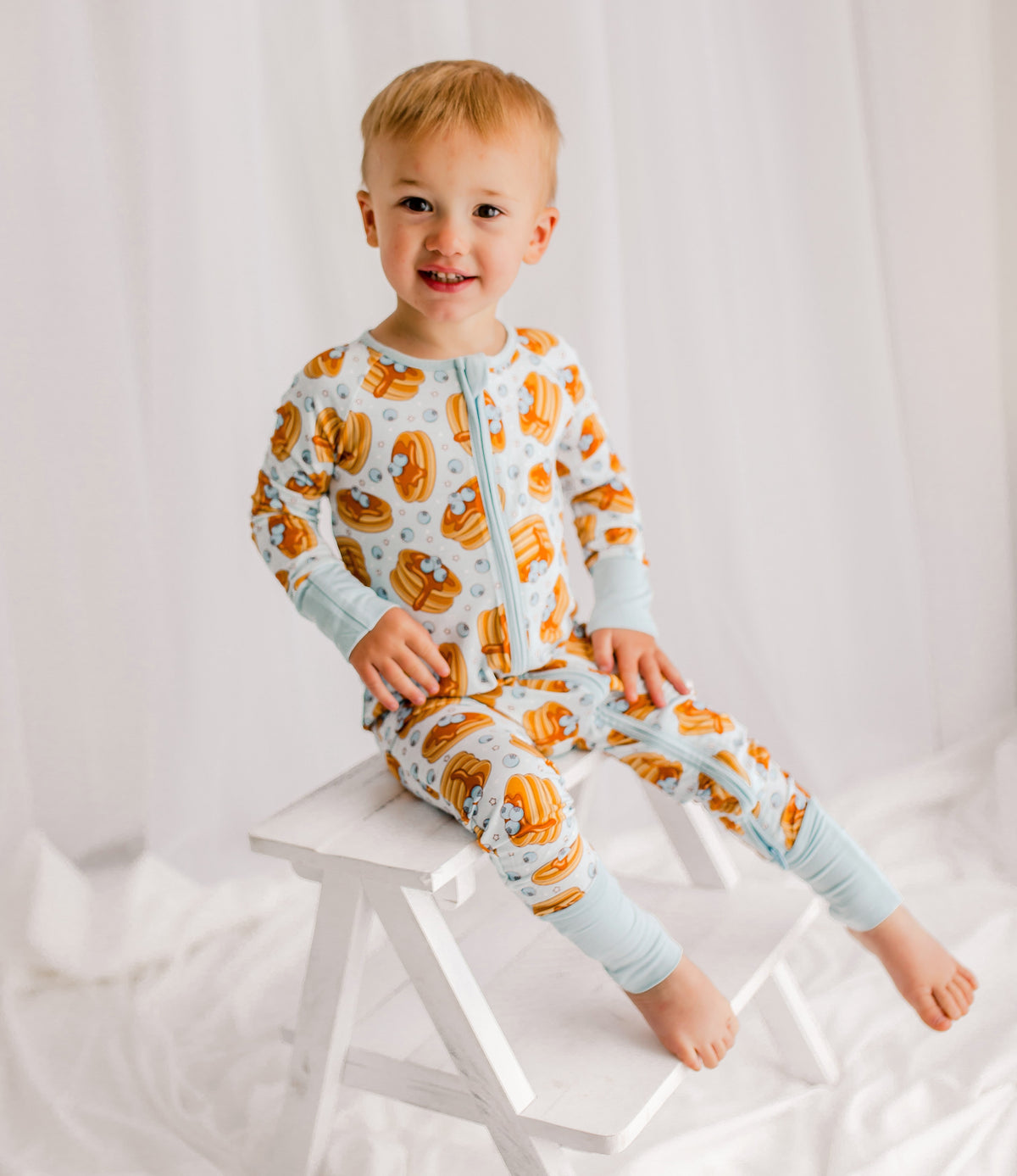 Child wearing light blue zippy with Maine blueberries, syrup, pancakes with light blue cuffs.