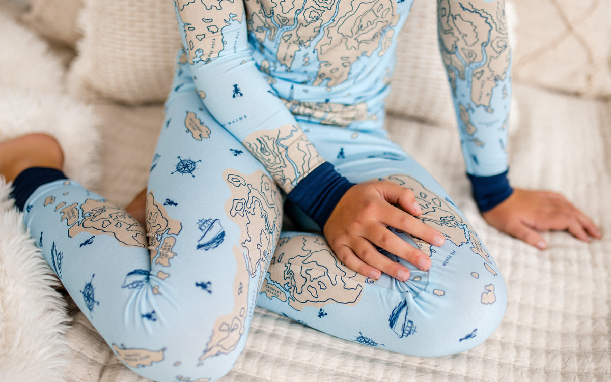 Child wearing light blue pajamas set that shows a nautical map of a piece of the Maine coast along with nautical symbols and the Atlantic Ocean