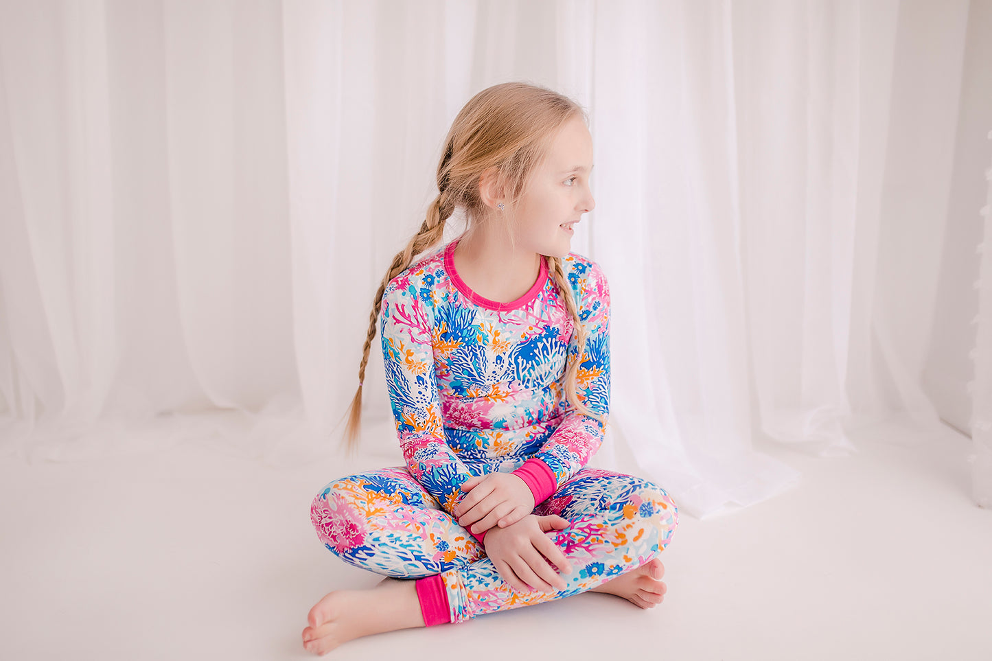 Child wearing Maine coral reefs with a white background with coral reefs in all different shades of pink, blue and white with pink cuffs.