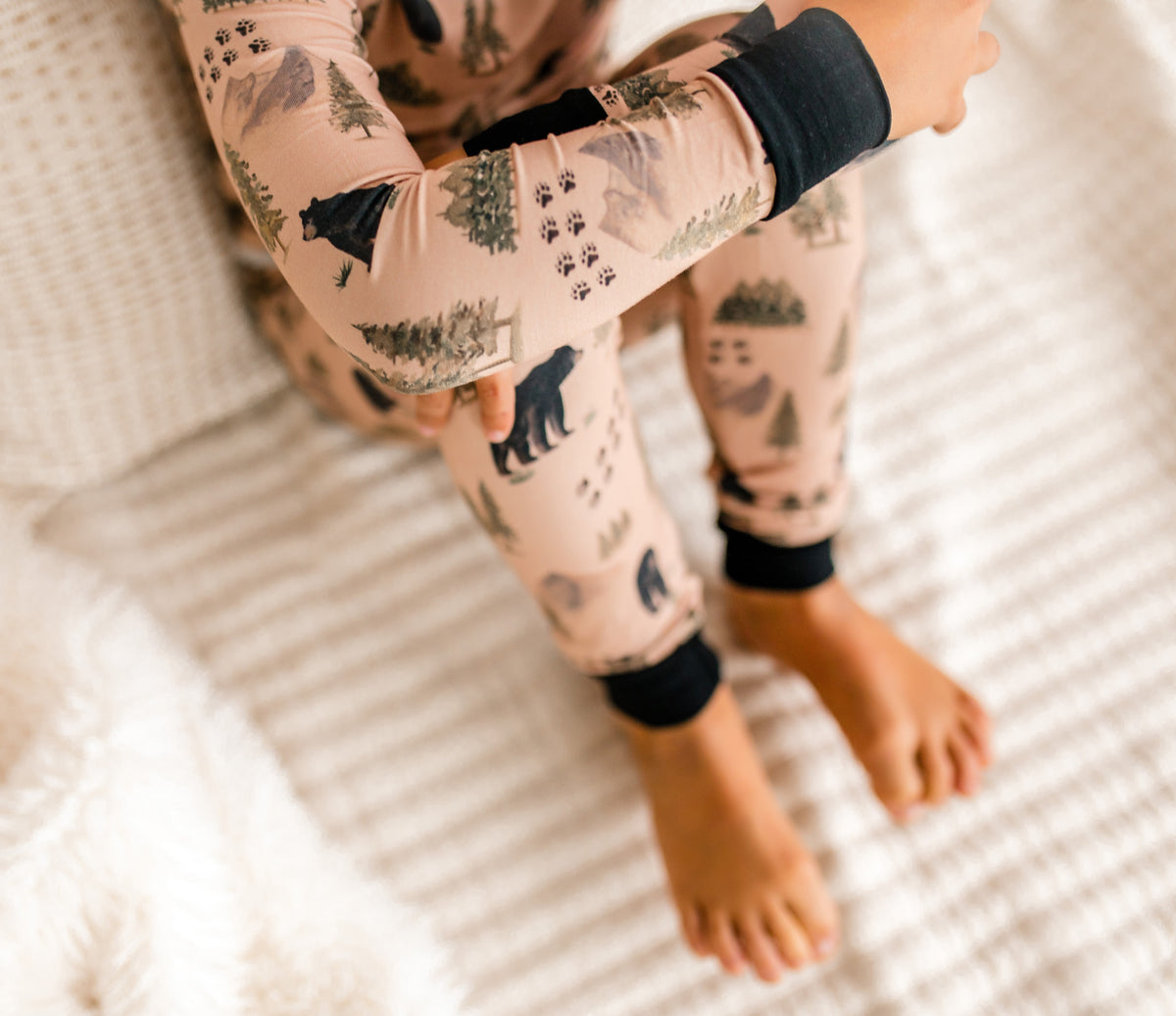 Child wearing tan pants with bears and their tracks and green trees and mountains with black accents