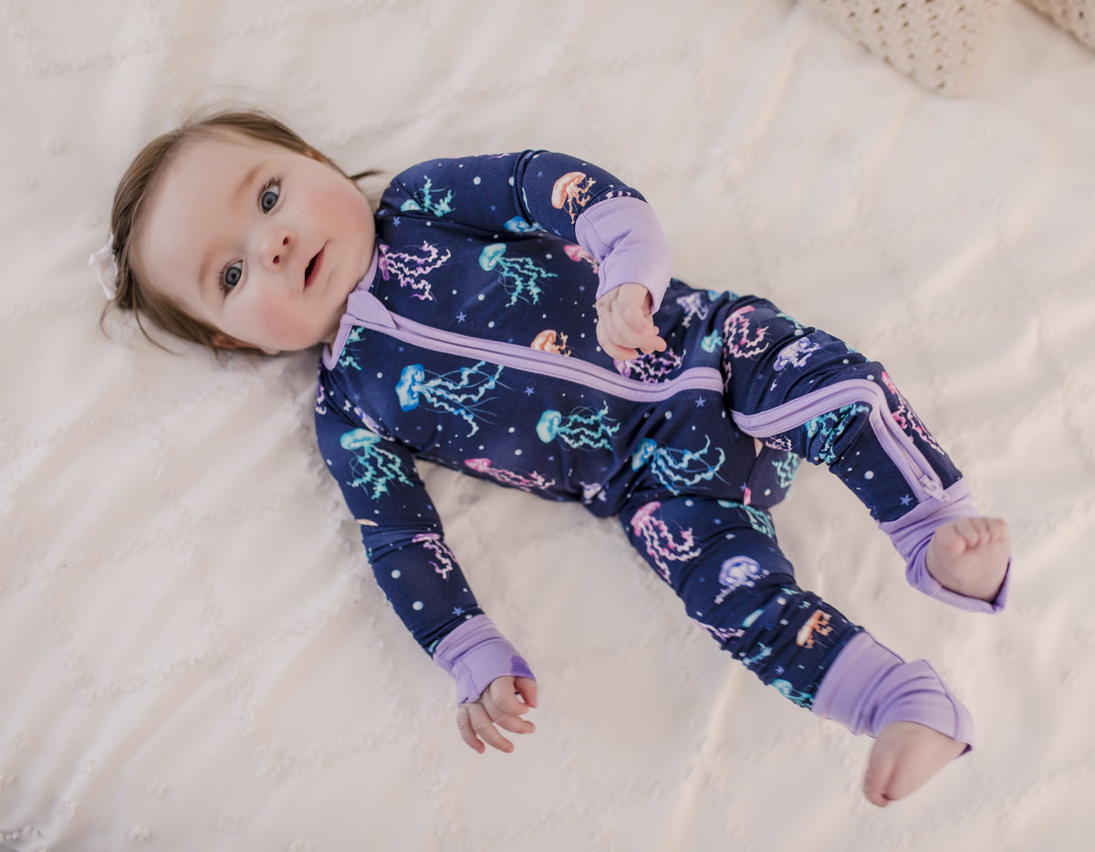 Baby wearing colorful jellyfish themed pajamas with tiny stars and circles with purple cuffs