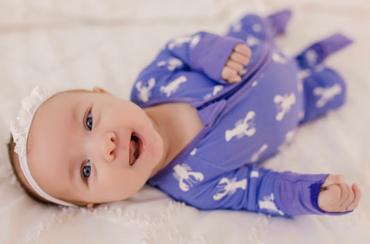 Baby wearing vibrant purple one piece pajama with white lobster pattern and purple cuffs