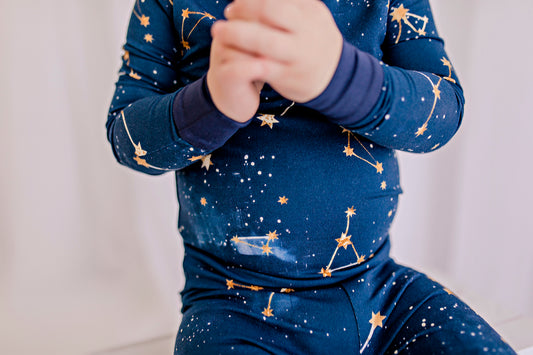 Child wearing a long sleeved dark blue pajama set with the little dipper and big dipper along with the galaxy and stars