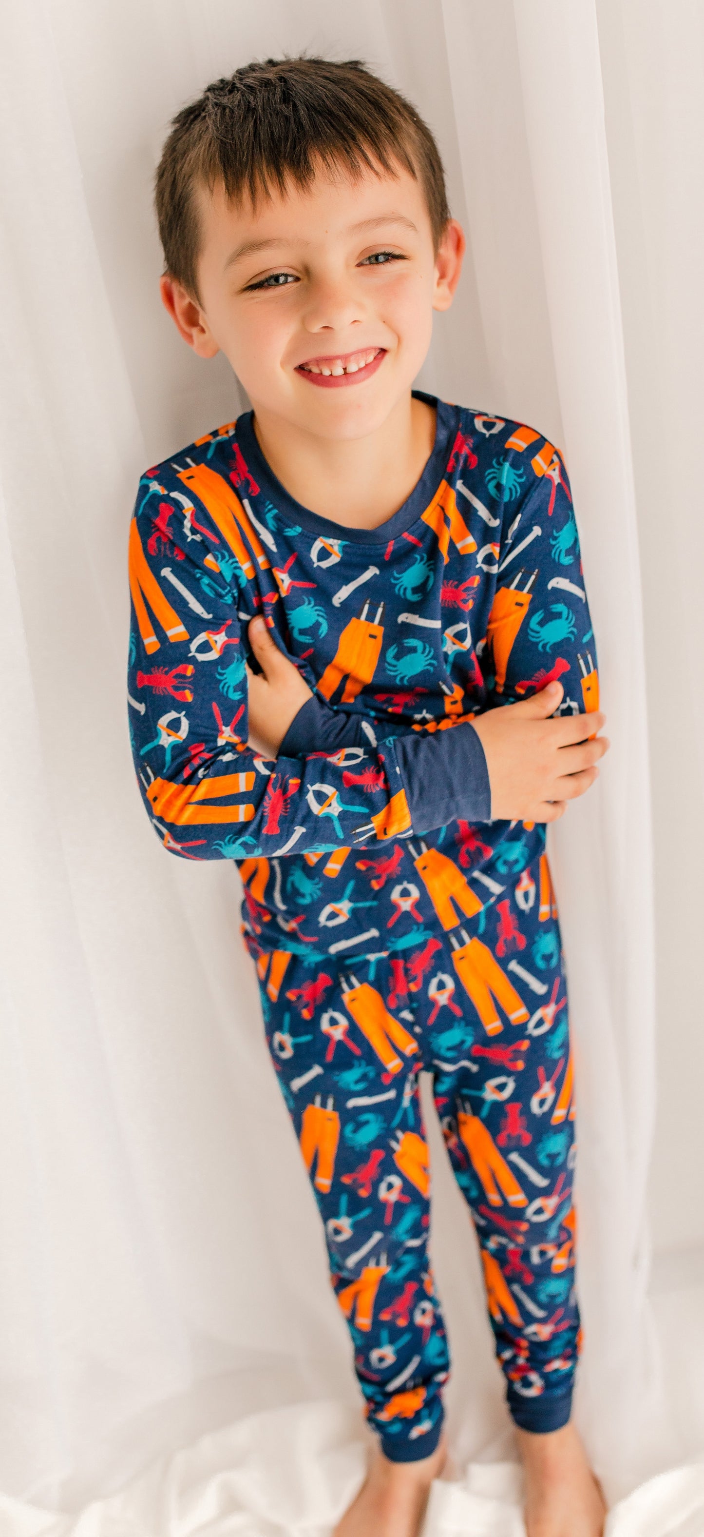 Child wearing a colorful pajama set with a blue background with lobsters, crabs, oil gear, banders, and measures.