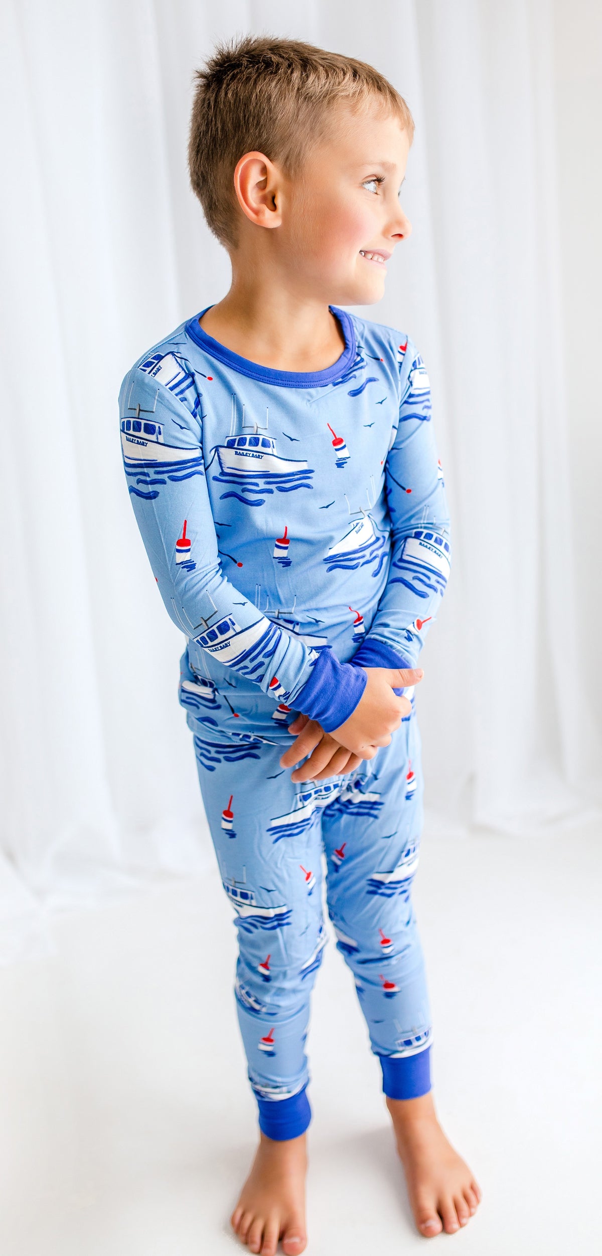 Child wearing blue two piece pajamas with boats and buoys floating, seagulls flying, and waves