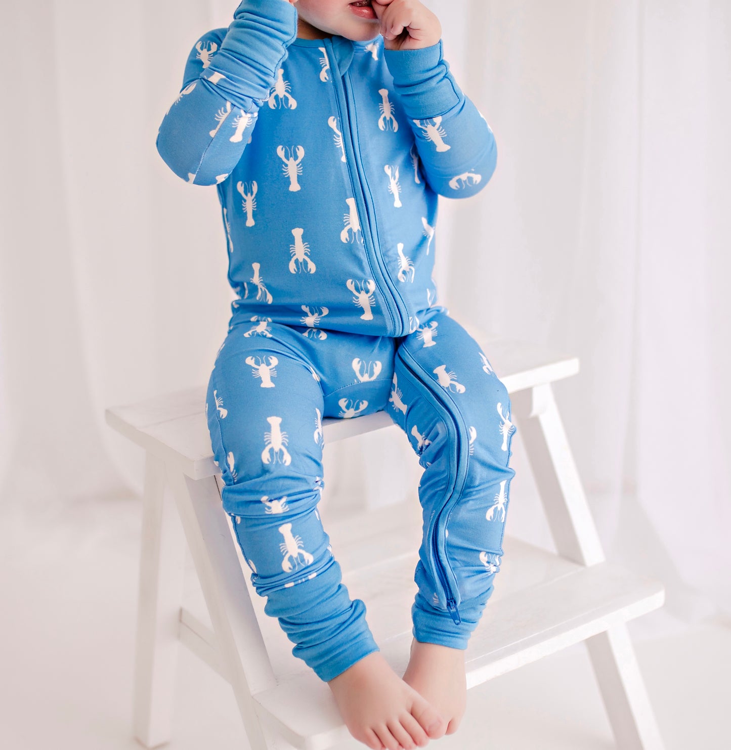 Child wearing light blue zippy romper the has white lobster pattern with blue cuffs