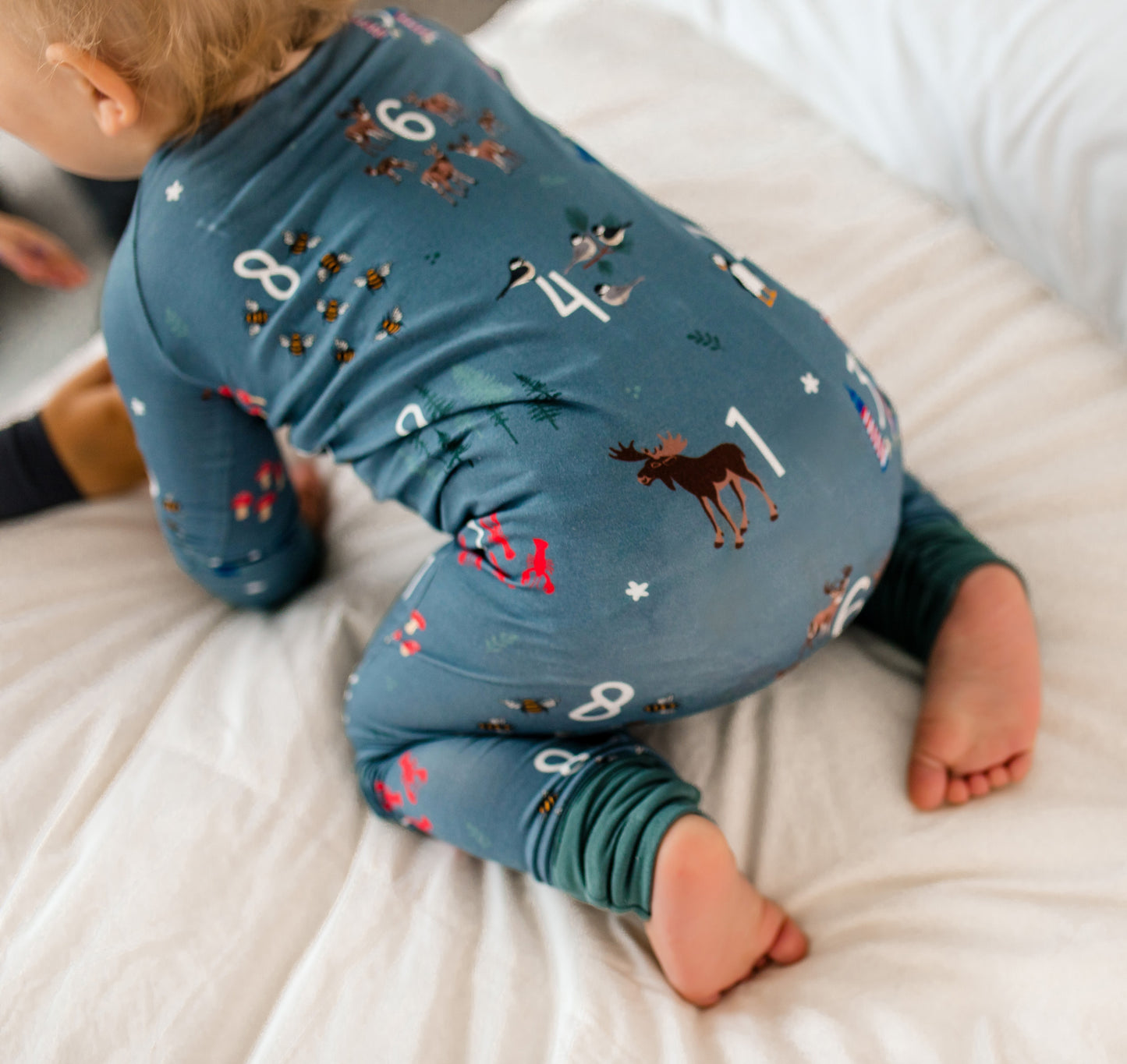Child wearing a gray onesie with numbers 1-10 and animals, along with blueberries and lobsters, which Maine is known for