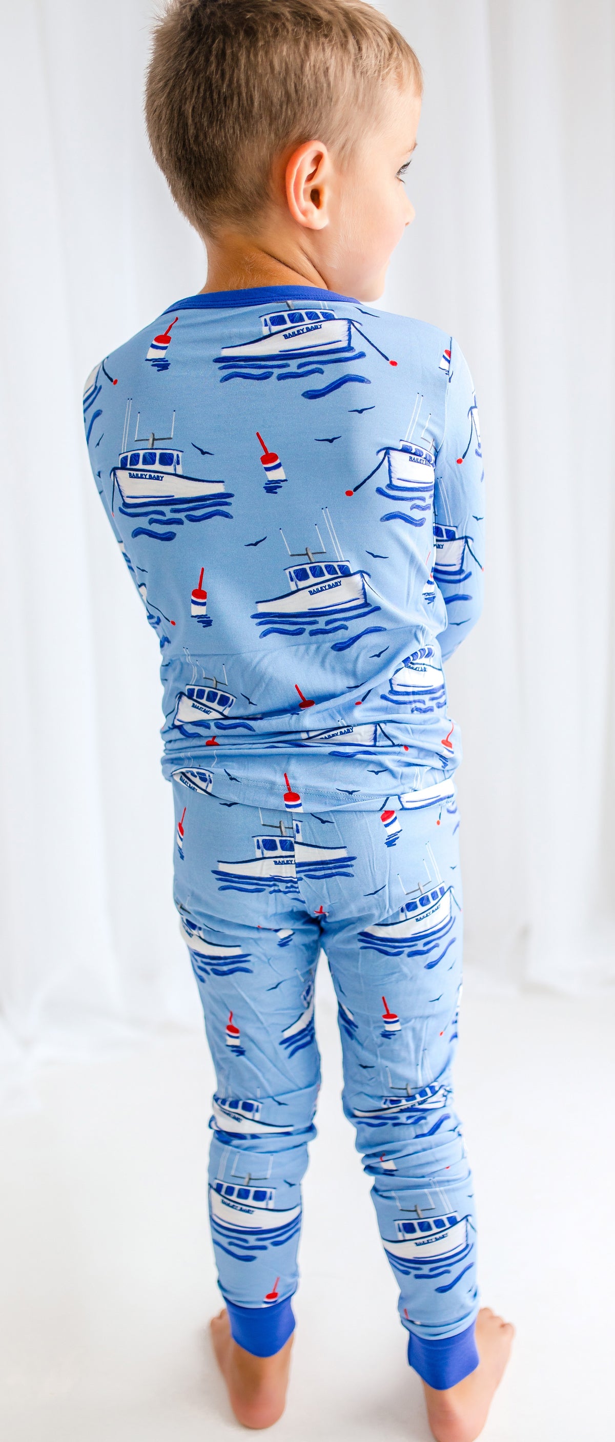 Child wearing blue pajamas with Maine fishing lobster boats, floating buoys, waves, and flying seagulls on the atlantic ocean