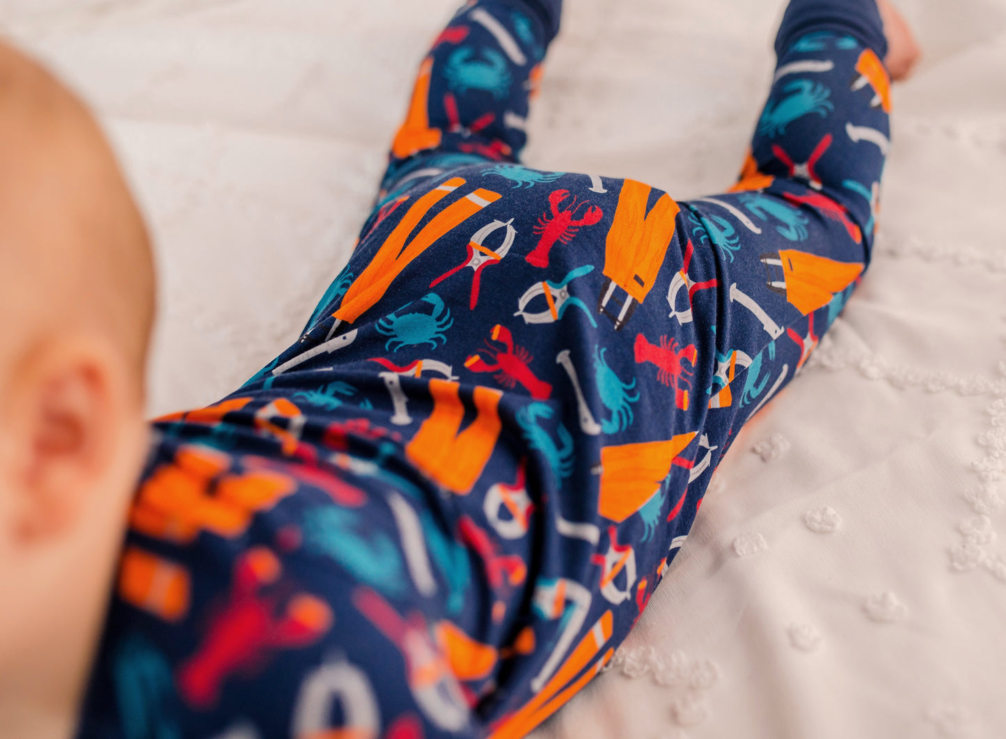 Baby wearing zippy that represents Maine lobster fishing with blue crabs, red lobsters, orange oil gear, and gray banders and measures.