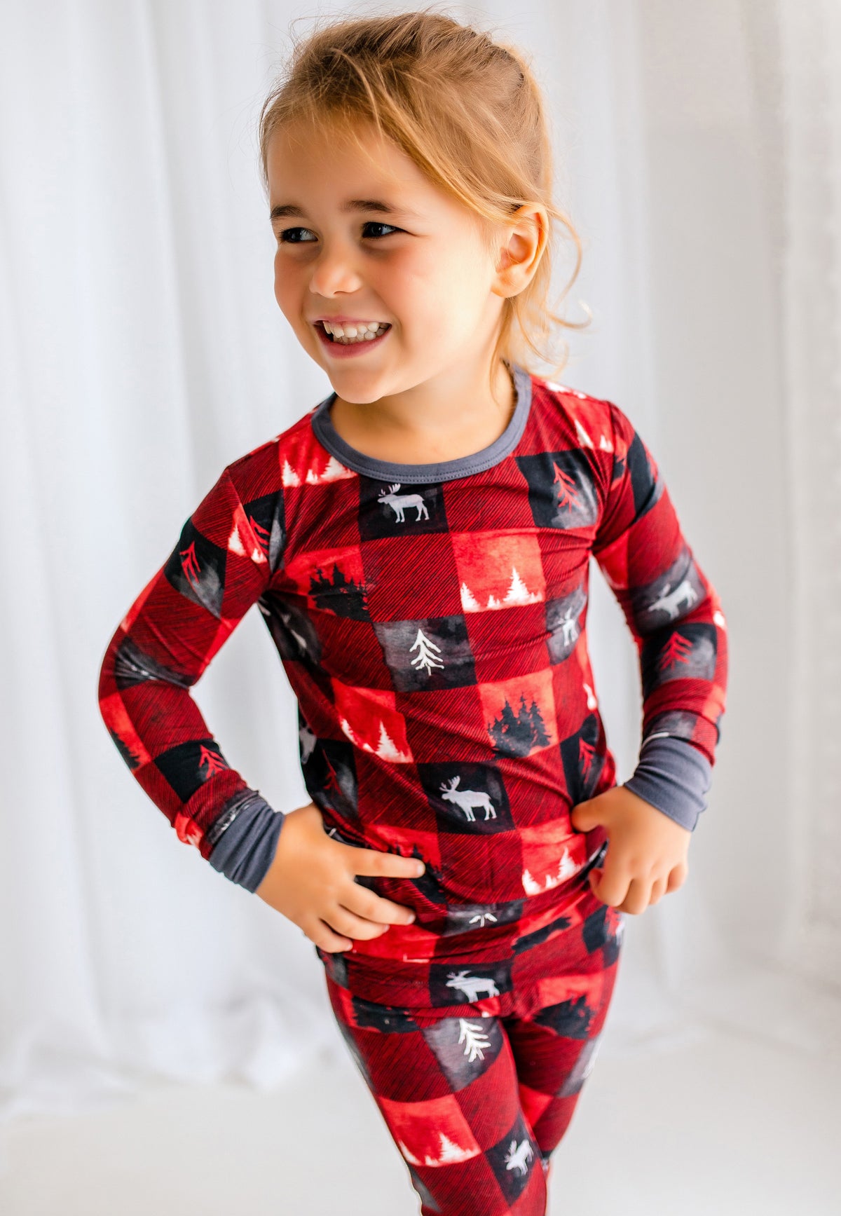 Child wearing red plaid two piece pajama set with trees from the Maine forest and white moose