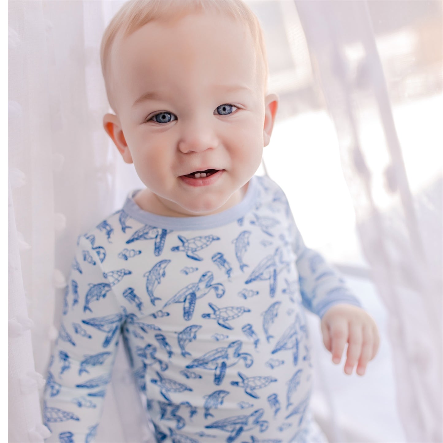 Child wearing light blue background pajama set with ocean animals like sea turtles and dolphins