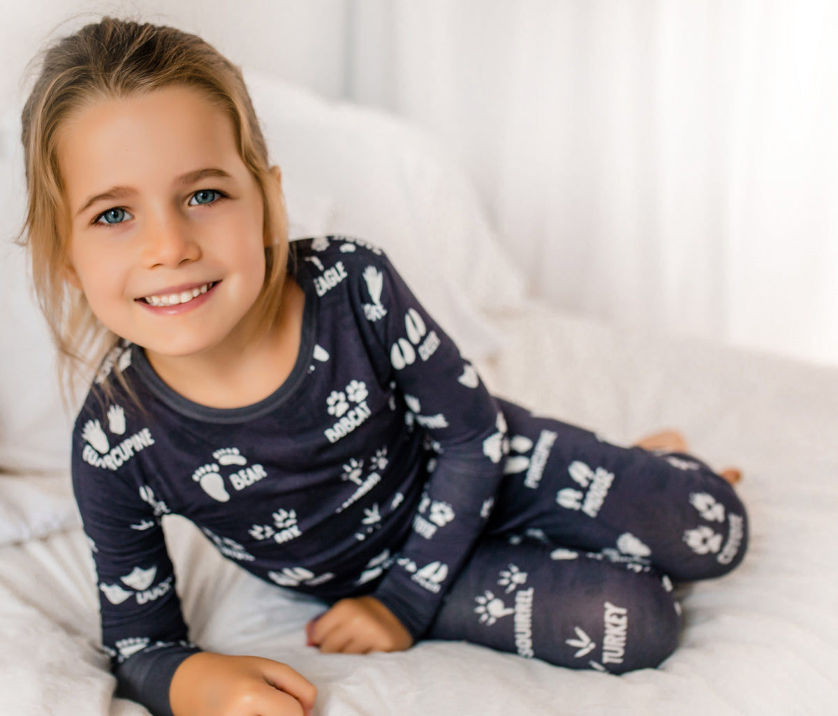 Child wearing dark grey pajamas with white animals tracks on a white blanket