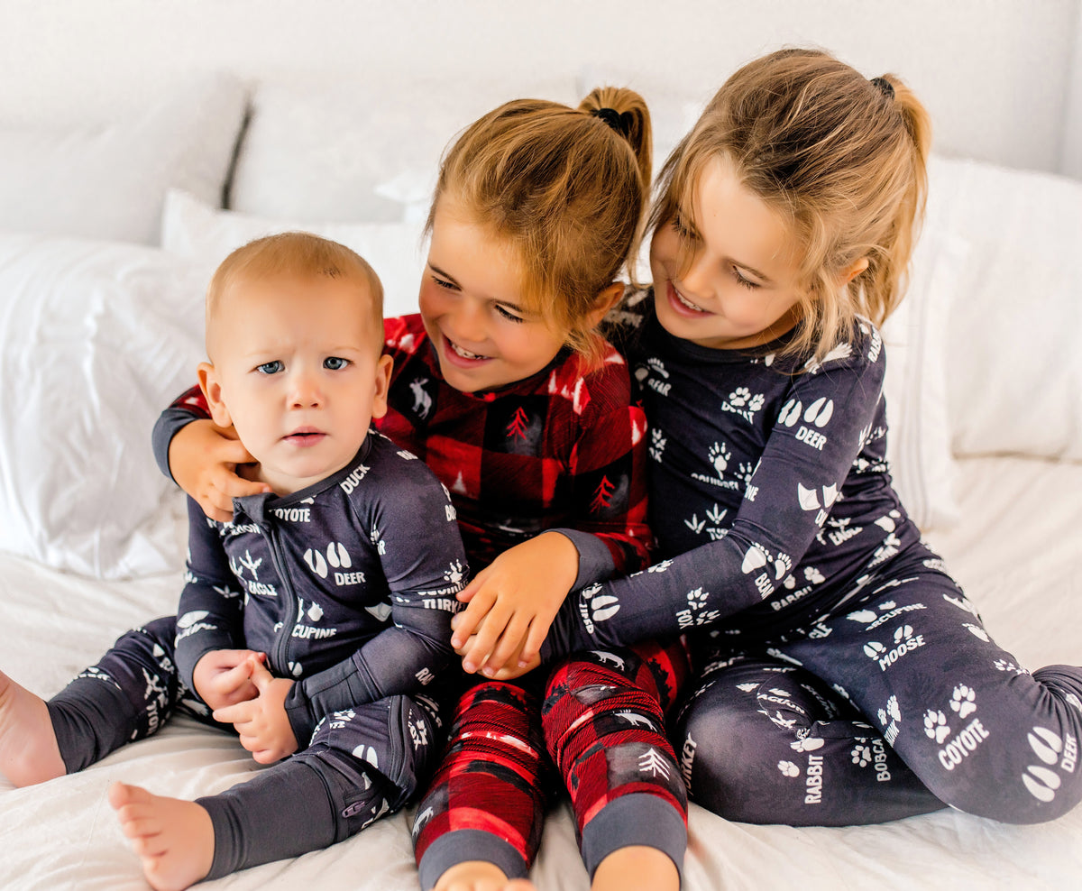 Three children in woodland themed bamboo pajamas sitting on a bed