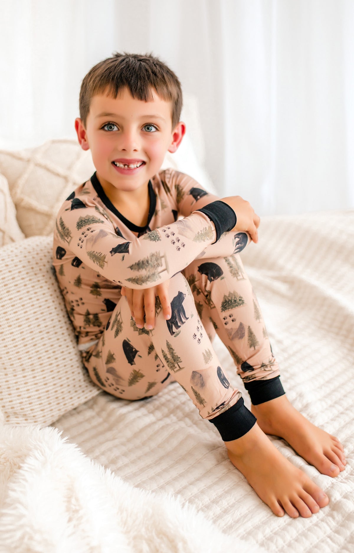 Child wearing pajamas with bear pattern, different trees of dark and light green with mountains