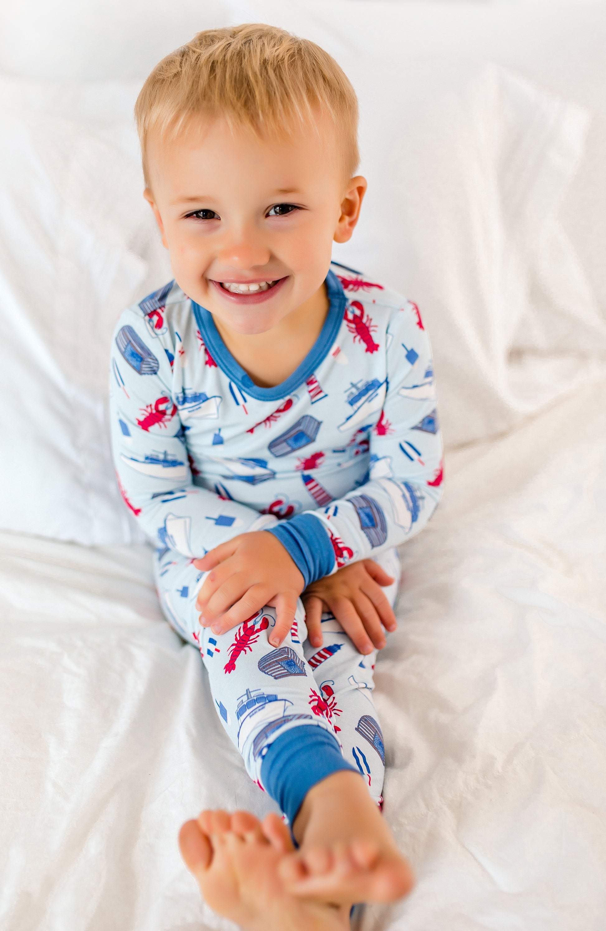 Child wearing colorful pajamas with a pattern, sitting on a white bed.
