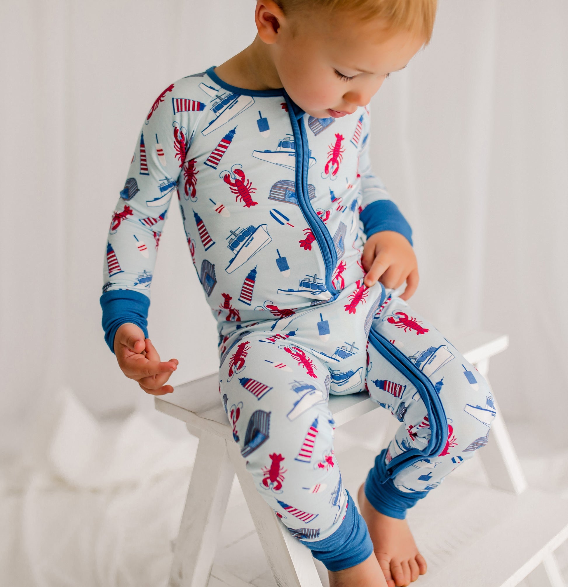Child wearing a light blue one piece with maine lobsters, traps, buoys, and boats with lighthouses and darker blue cuffs 