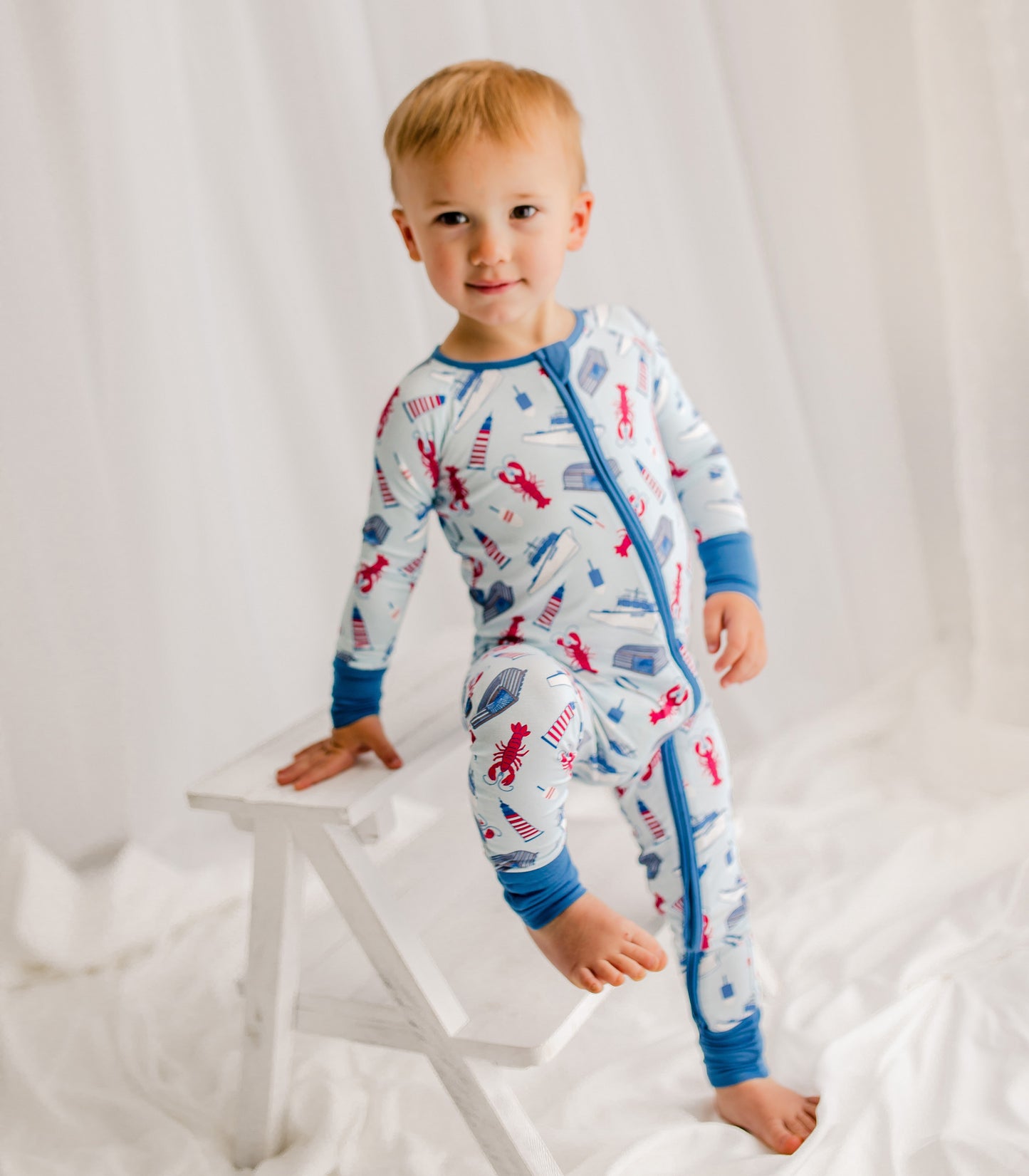 Child wearing a patterned onesie featuring maine lobsters, boats, lighthouses, and buoys 