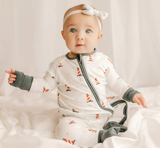 Baby wearing a one piece zippy romper with black cuffs, a white background, and red and white lighthouses all over 