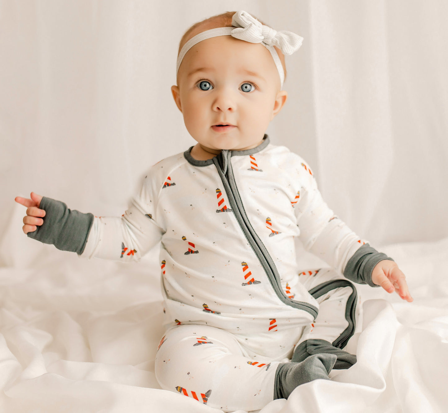Baby wearing a one piece zippy romper with black cuffs, a white background, and red and white lighthouses all over 