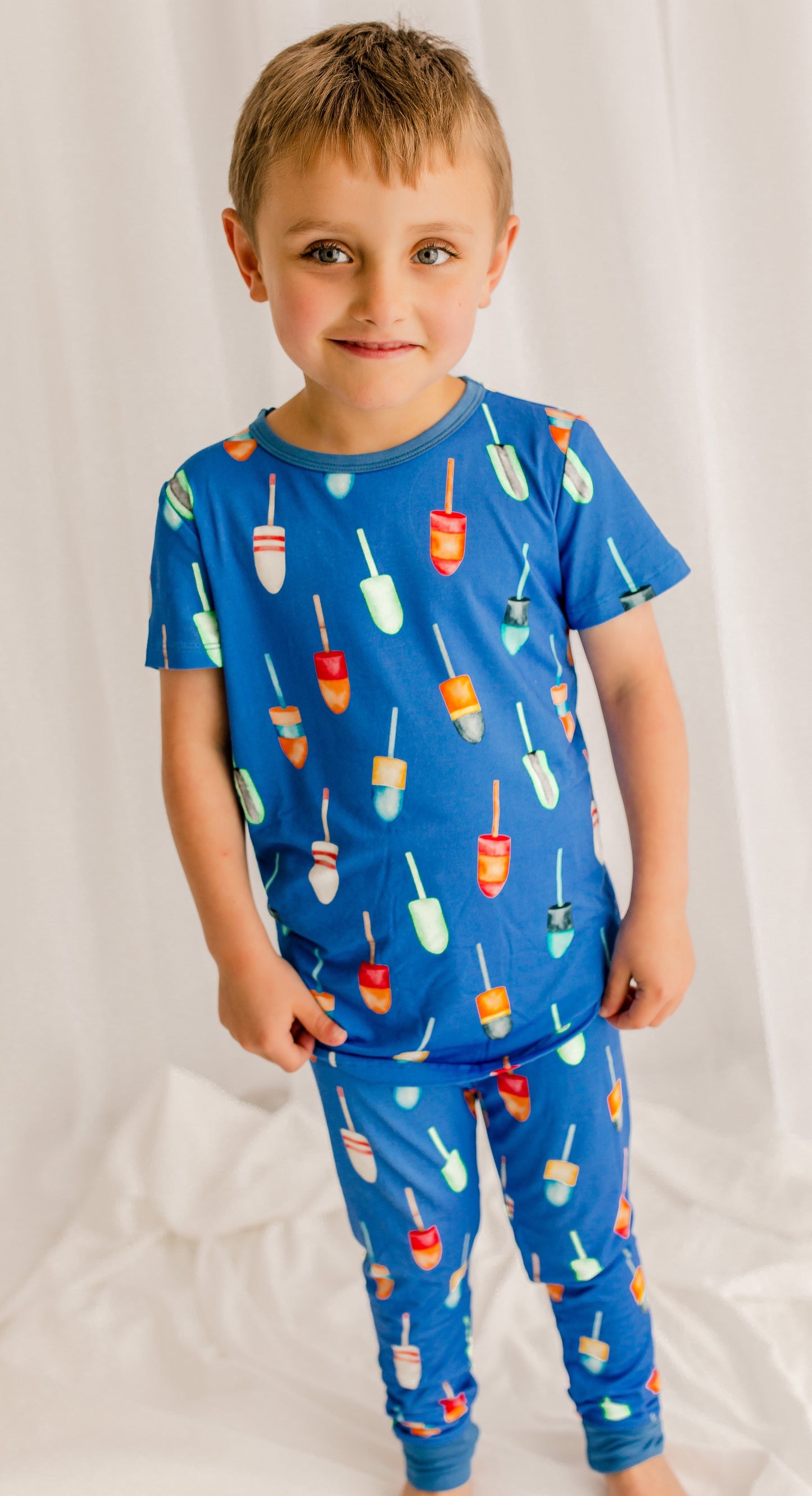 Child wearing a blue pajama set with colorful buoys all over 