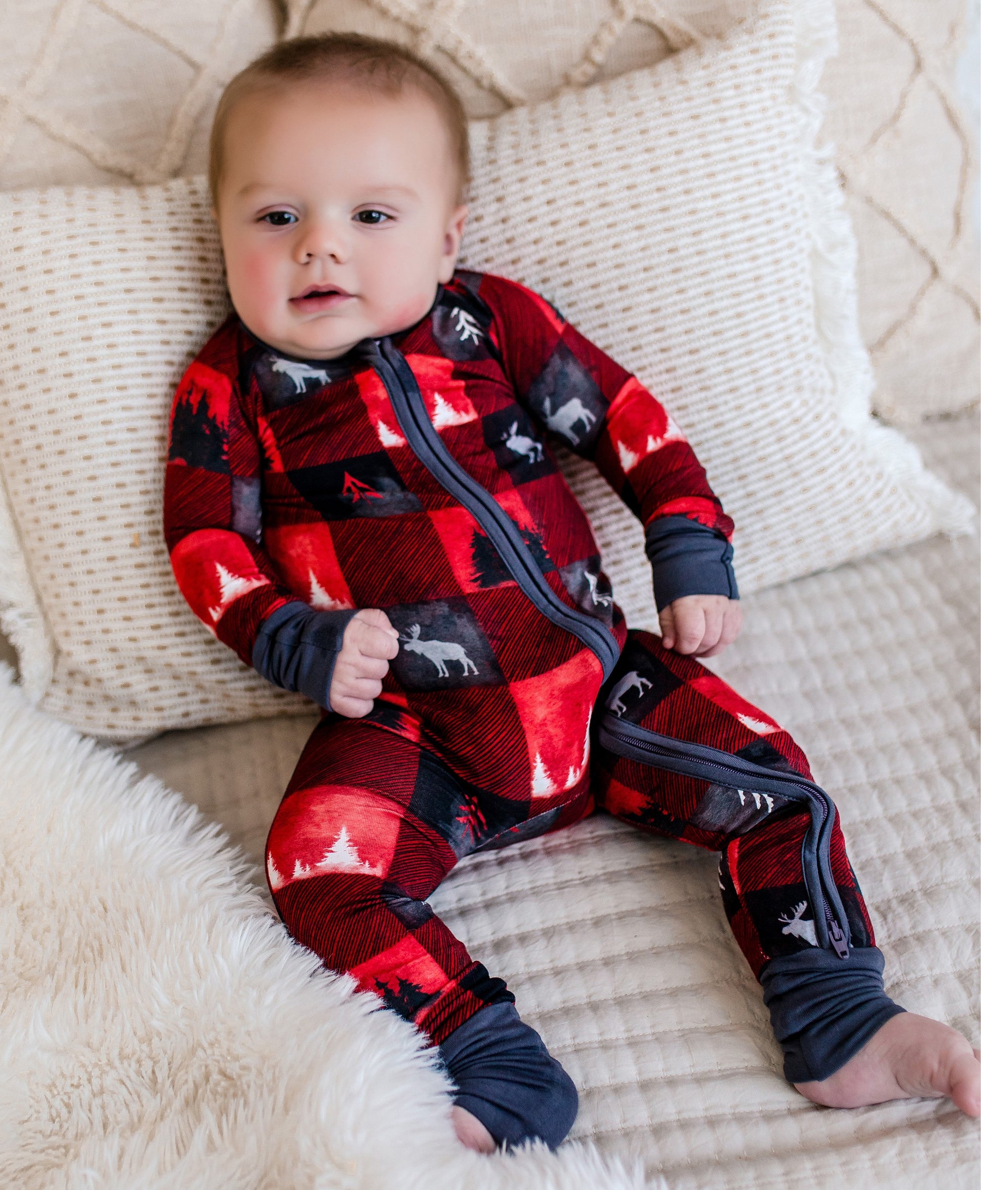 Baby wearing a red and black plaid onesie with images of trees in black and white and a white moose 