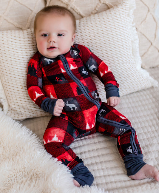 Baby wearing a red and black plaid onesie with images of trees in black and white and a white moose 