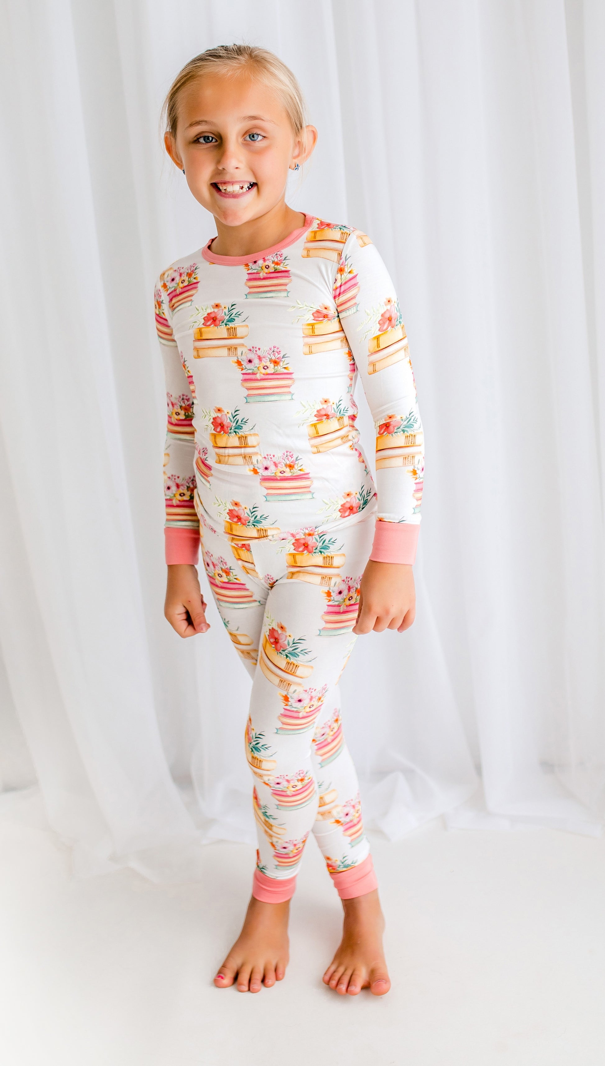 Child wearing a colorful two piece with floral prints and stacks of book on a white background with pink accents 