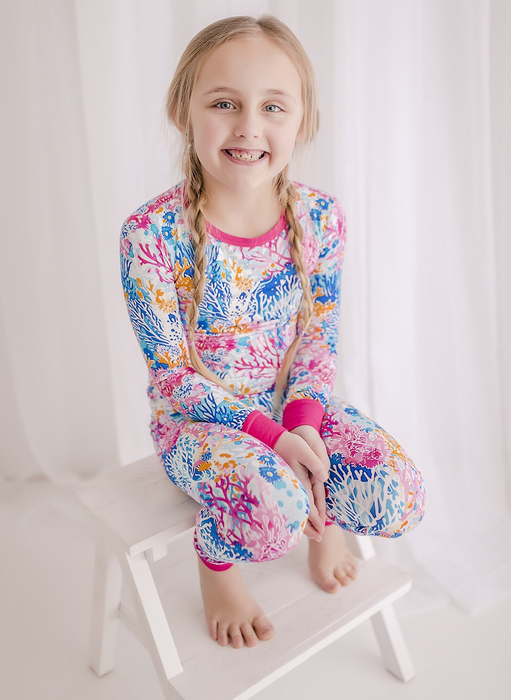 A child wearing a long sleeve top and pants with a vibrant coral reef design in multiple pink shades along with different blues and oranges. 