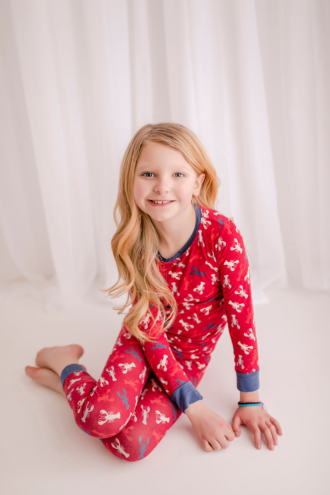 Close-up of child wearing red Maine lobster themed pajamas with all-over lobster print and contrast cuffs