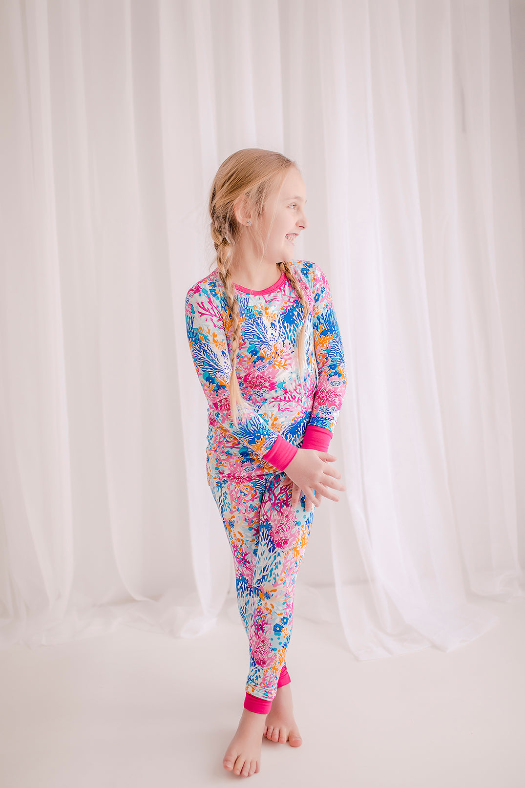 Child wearing colorful two piece pajama set with coral reefs of all different shades of pink, blue, and orange 