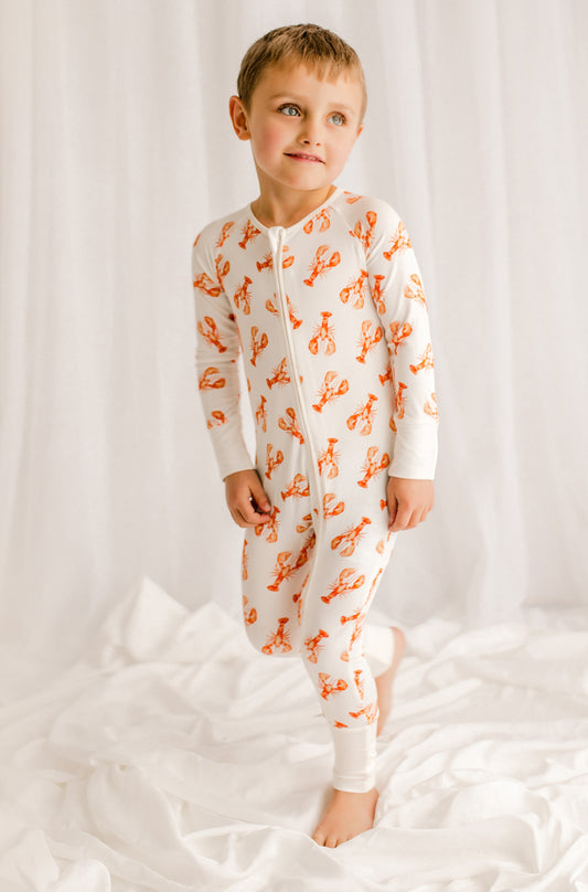 Child wearing a white onesie with orange lobster pattern against a white background