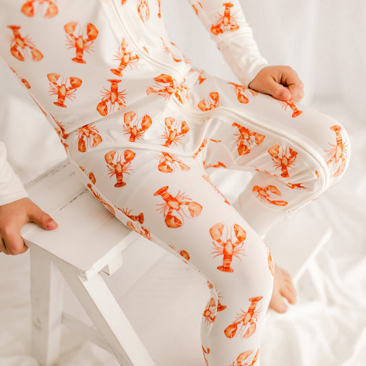 Child wearing a white one piece with orange lobster patterns on a white background