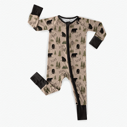 Baby onesie with bear and forest patterns along with animal tracks on a tan background with black accents 