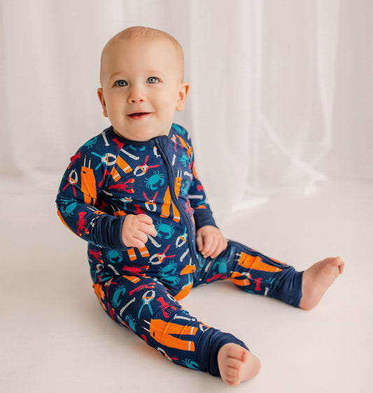 Baby wearing a colorful one piece with oil pants, crabs, lobsters, and tools for working on a fishing boat 