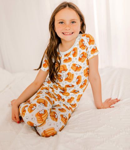 Young girl wearing a short sleeve pajama set with Maine blueberries on a stack of pancakes with syrup dripping down 