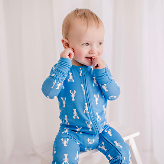 A baby wearing a blue lobster print romper with zipper detailing.
