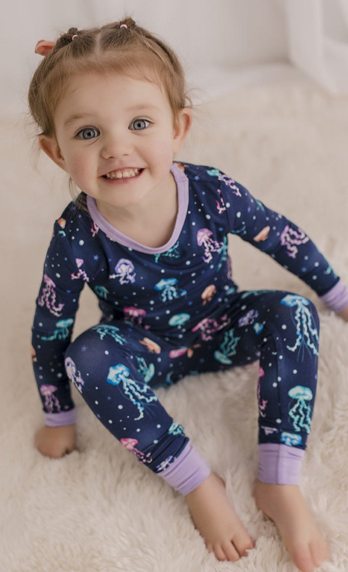 Child wearing a dark blue pajama set with vibrant colors of one of the prettiest maine  ocean animals with purple cuffs 
