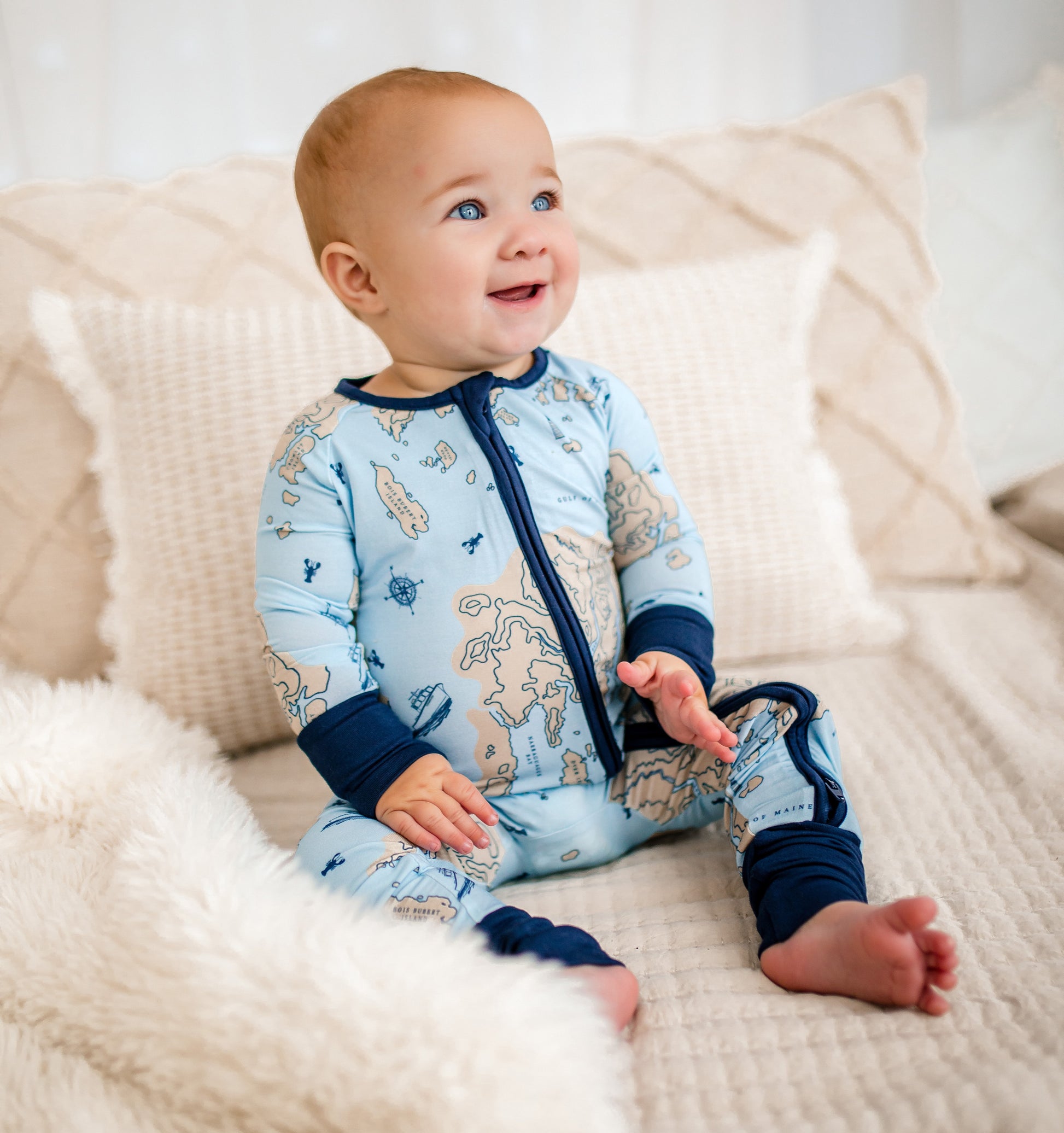 Baby wearing a light blue one piece with a nautical chart of the maine coastline and atlantic ocean 