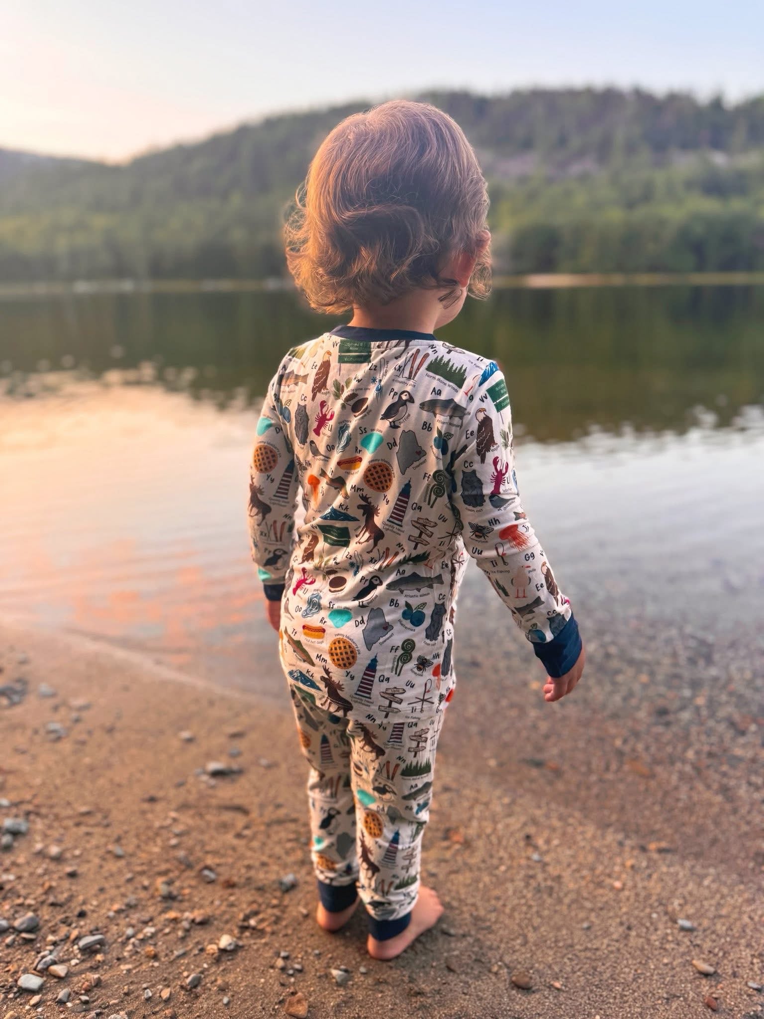 Child in pajamas standing by a in Maine with items on the pajamas to represent all the things that make up maine 