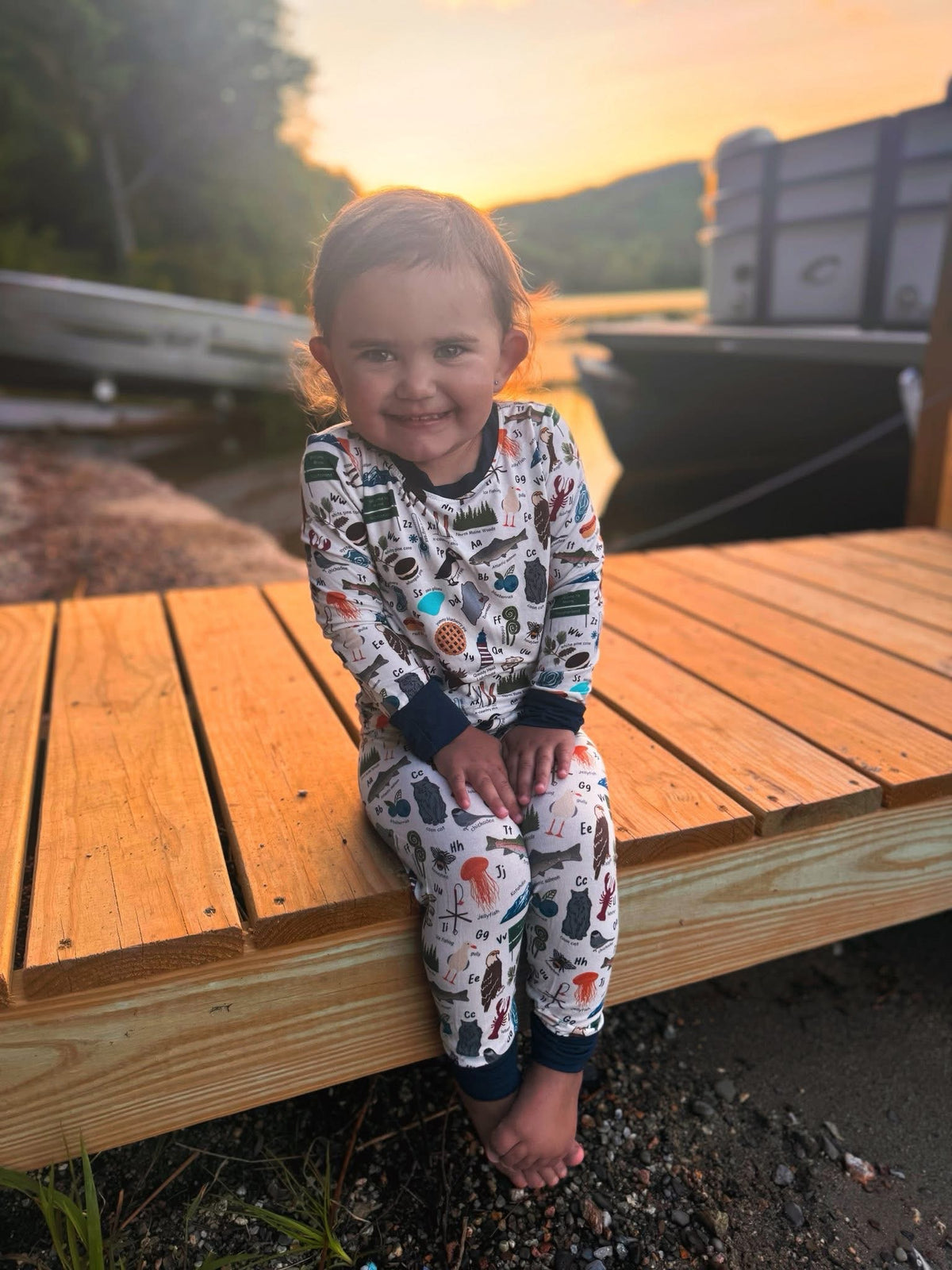 Child wearing long sleeved two piece pajama set with maine items all over to make up the maine alphabet 