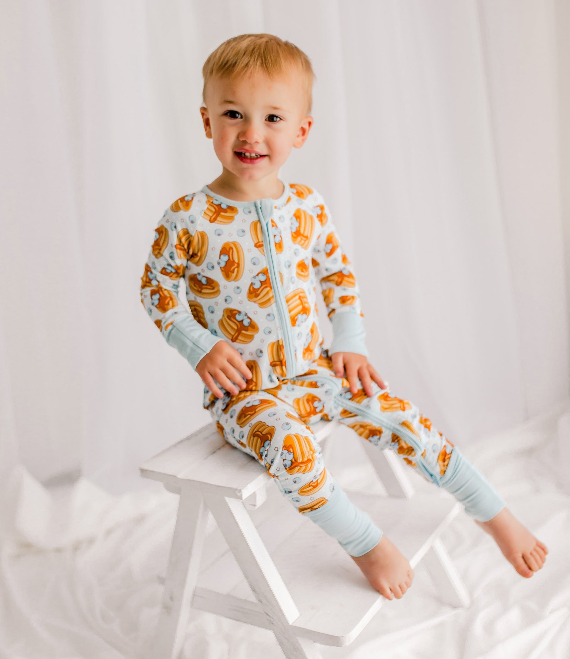 Child wearing light blue zippy with Maine blueberries, syrup, pancakes with light blue cuffs. 