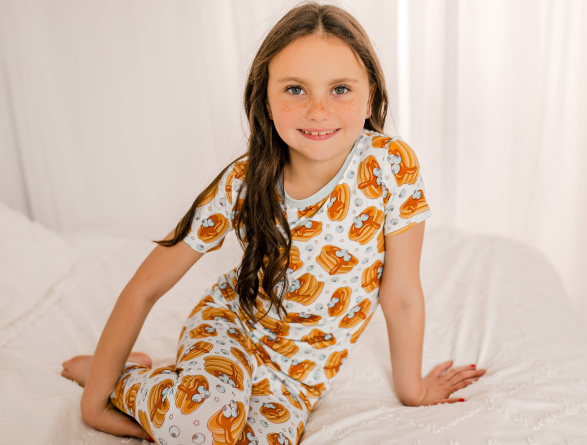 Young child wearing stacks of pancakes with syrup dripping down and maine blueberries on top with cream colored little stars all over 