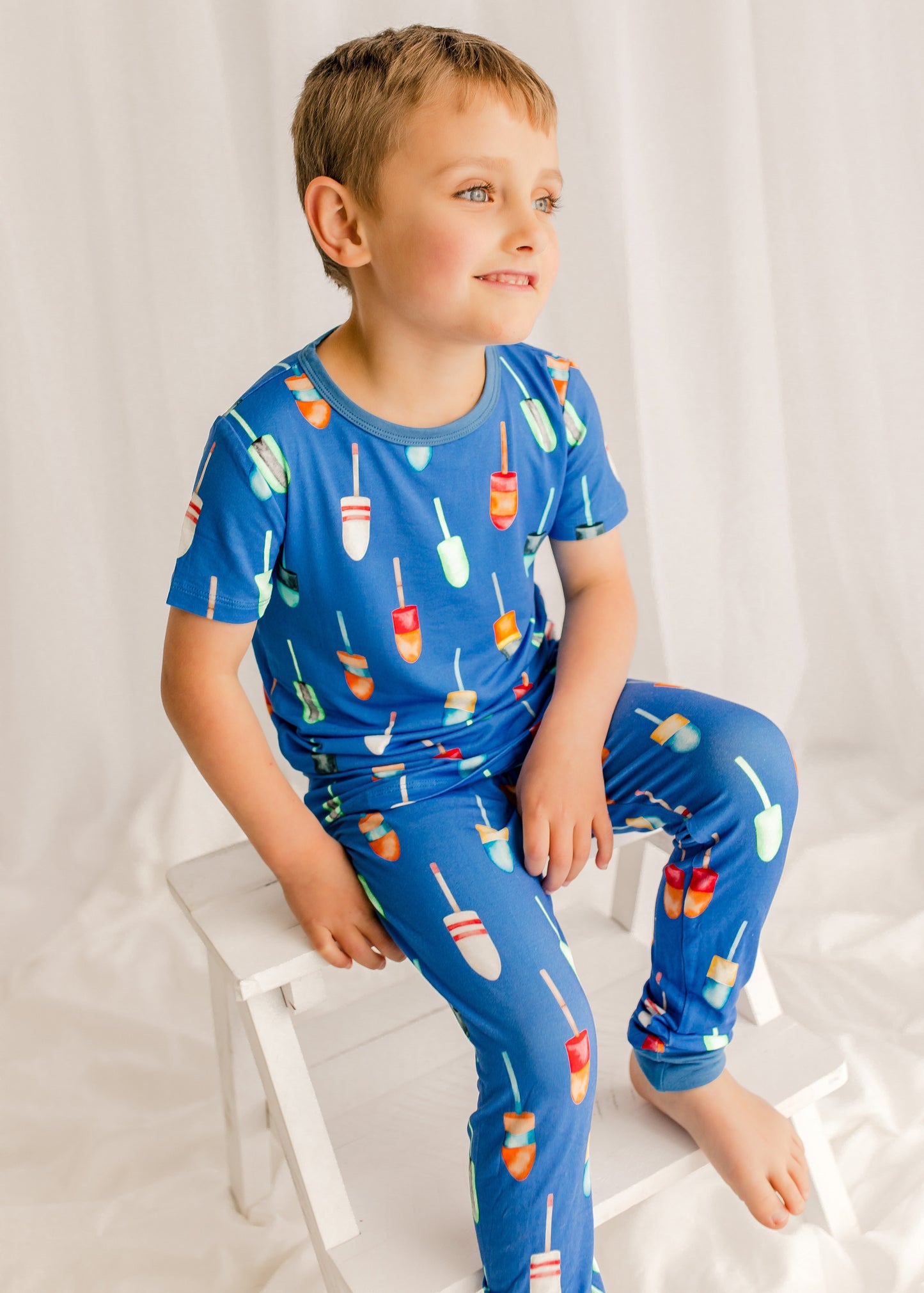 Child wearing short sleeved top and long pants with a blue background with all kinds of colorful buoys 