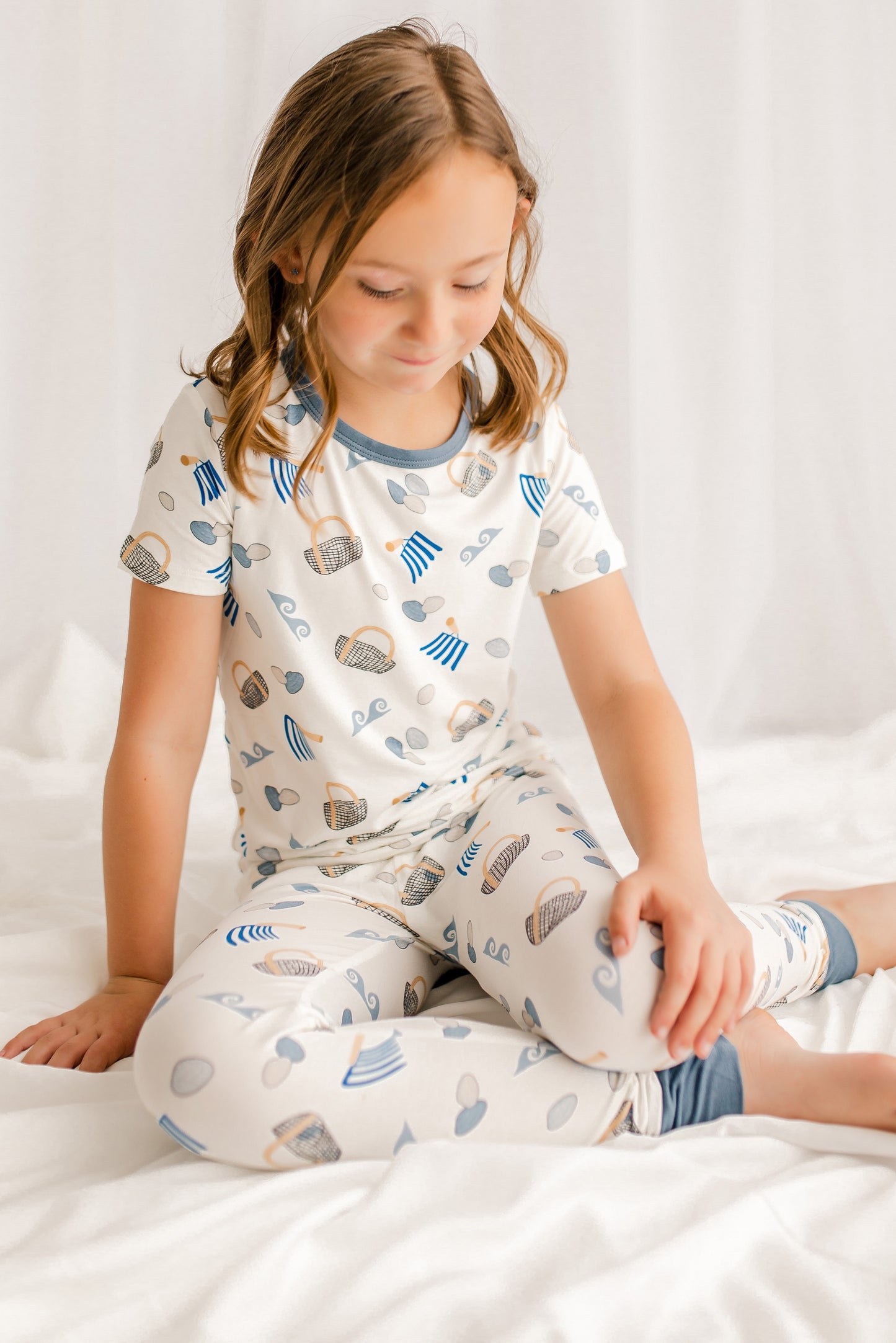 Child wearing a short sleeve pajama set with clams, diggers, baskets, and waves with gray cuffs on a white background 