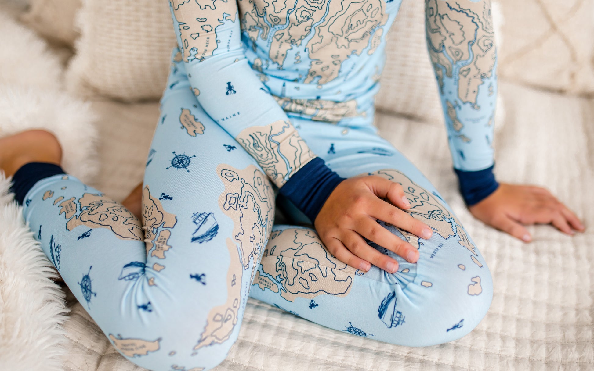 Child wearing light blue pajamas set that shows a nautical map of a piece of the Maine coast along with nautical symbols and the Atlantic Ocean 