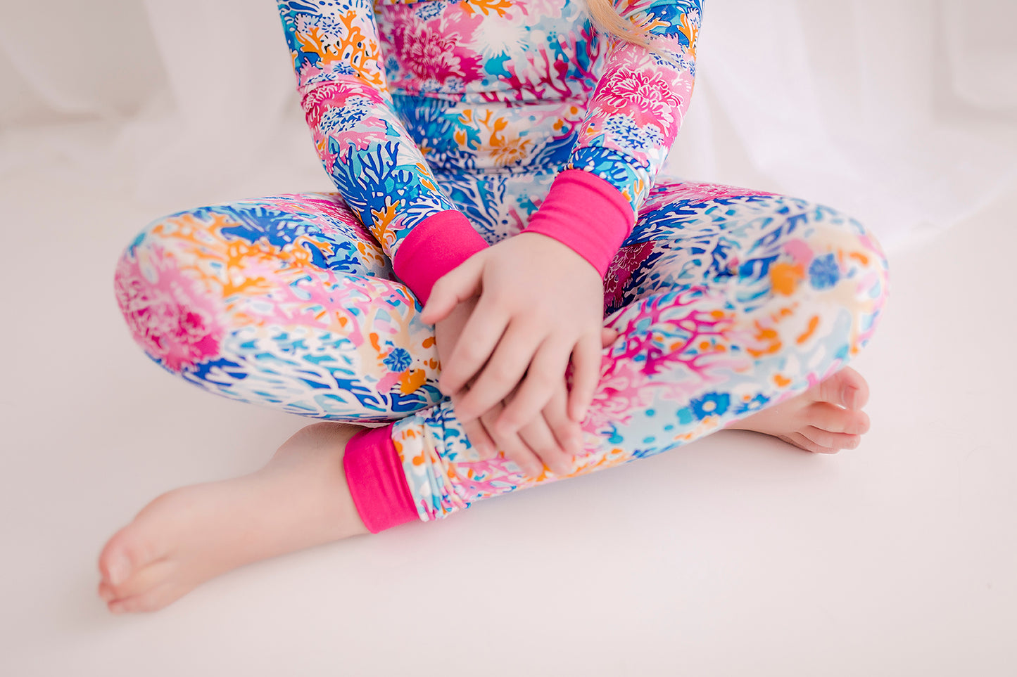 Child wearing colorful two piece pajama set with coral reefs of all different shades of pink, blue, and orange 
