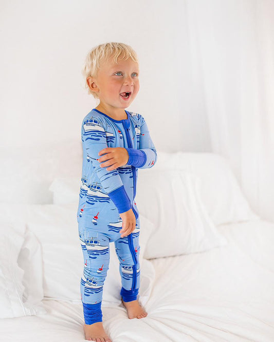 Child wearing blue pajamas with floating boats and buoys, on the atlantic ocean with seagulls flying in the sky 